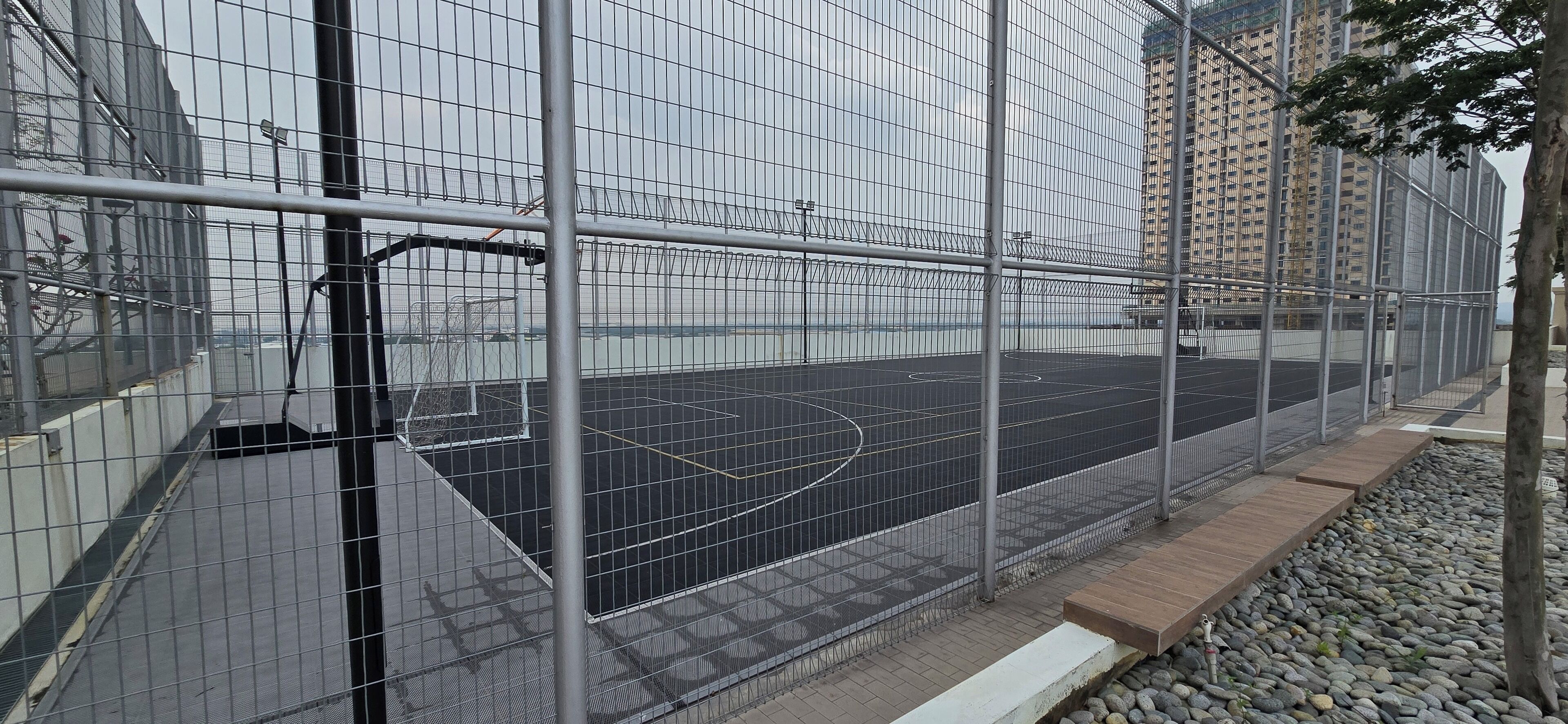 A basketball court enclosed by a metal fence, with a building in the background.