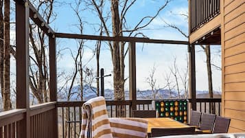 Une terrasse en bois avec un jacuzzi, une table et des chaises, et une vue sur les montagnes.