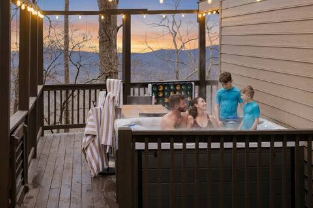 Un bain à remous avec une vue imprenable sur les arbres et les montagnes, une terrasse en bois et des guirlandes lumineuses.