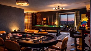 Een pooltafel met biljartaccessoires, een bar met krukken, en een uitzicht op de stad door grote ramen.