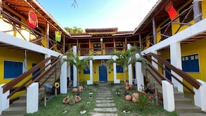 Un cortile con un percorso centrale, circondato da edifici dalle pareti giallo e blu, ringhiere in legno e piante in vaso.