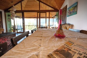 A dining table with a newspaper spread, wooden chairs, and a large window with a view of the outdoors. - VİTA CAMPING (Konyaalti)