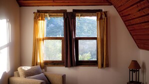 A room with a bed, a chair, and a lamp. There are two windows with curtains.