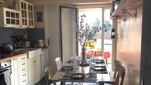 A modern kitchen with white cabinets, a dining table set for four, and a view of the outdoors through a large window. - Large apartment in a quiet area, 2 terraces. (Biarritz)
