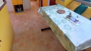 A compact kitchen with a dining area, featuring a table with a floral tablecloth, yellow cabinets, and a television mounted on the wall. - Gorges du verdon M.H. Eden34 camping3*, swimming pool, in the middle of lavender fields (Sainte-Croix-du-Verdon)