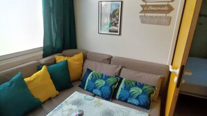 A living room with a sofa, pillows, a table with a decorative item, a framed picture, and a wall sign. - Gorges du verdon M.H. Eden34 camping3*, swimming pool, in the middle of lavender fields (Sainte-Croix-du-Verdon)