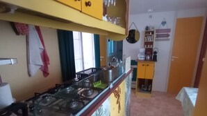A kitchen with yellow cabinets, a gas stove, and a countertop with various items. - Gorges du verdon M.H. Eden34 camping3*, swimming pool, in the middle of lavender fields (Sainte-Croix-du-Verdon)