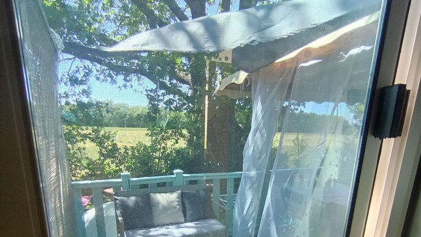 A screened patio area with a cushioned seating arrangement and a small table, overlooking a garden with trees and a fence. - Gorges du verdon M.H. Eden34 camping3*, swimming pool, in the middle of lavender fields (Sainte-Croix-du-Verdon)