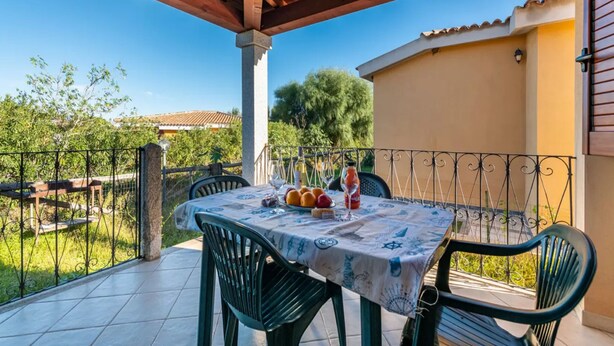 A covered patio with a table set for dining, surrounded by a metal fence and greenery. - Charming Detached Villa in Capo Comino (Siniscola)