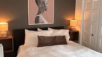 A bedroom with a bed, two bedside lamps, a door, and a wall-mounted artwork.