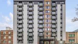 Um edifício residencial com vários andares, varandas, uma entrada central e fachada de tijolo.