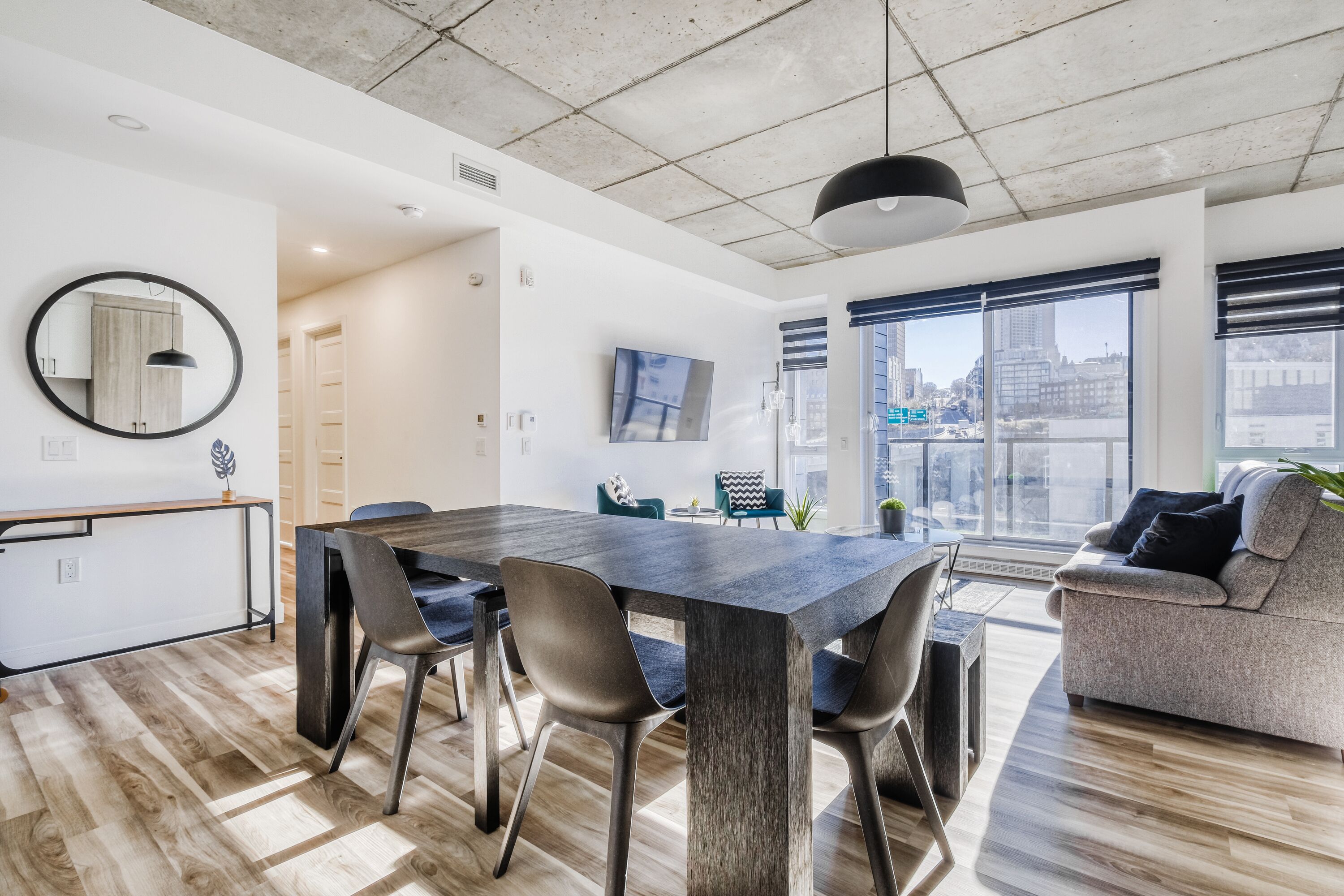 Un salon moderne doté d’une grande table à manger, de sièges confortables, d’un téléviseur à écran plat et d’une grande fenêtre offrant une vue sur la ville.