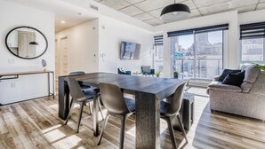 Sala de estar moderna com uma grande mesa de jantar, assentos confortáveis, uma TV de tela plana e uma janela ampla com vista para a cidade.