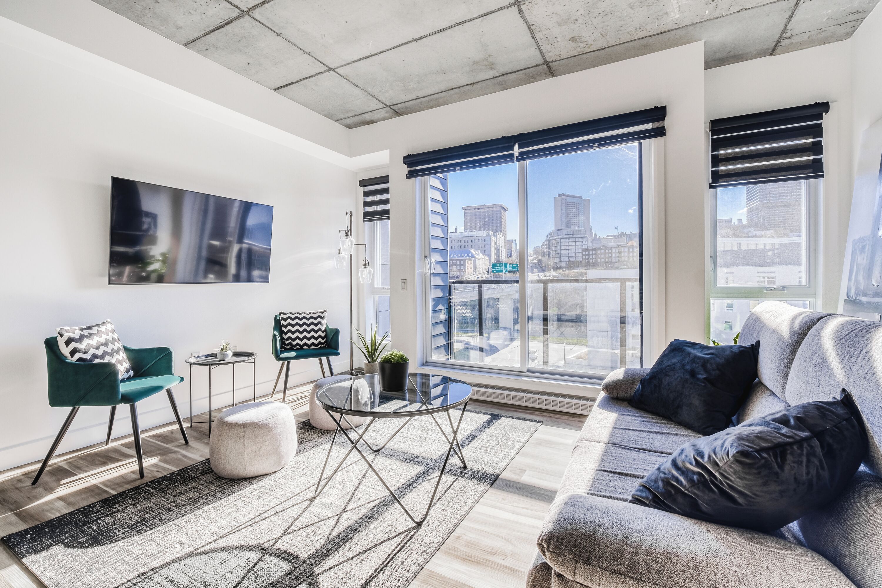 Un salon moderne avec un canapé, des fauteuils, une table basse et une grande fenêtre équipée de stores.