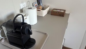 Eine Küchenzeile mit Kaffeemaschine, einem Korb mit Brot, einer Schachtel mit der Aufschrift „TEE“ und einer Rolle Küchenpapier.