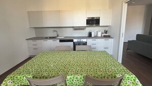 Eine kleine Küche mit weißen Schränken, einem Einbauofen und einem Essbereich mit einem Tisch, bedeckt mit einer grün gemusterten Tischdecke.