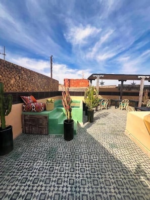 En takterrass med ett mönstrat golv, en stenmur och en träpergola.