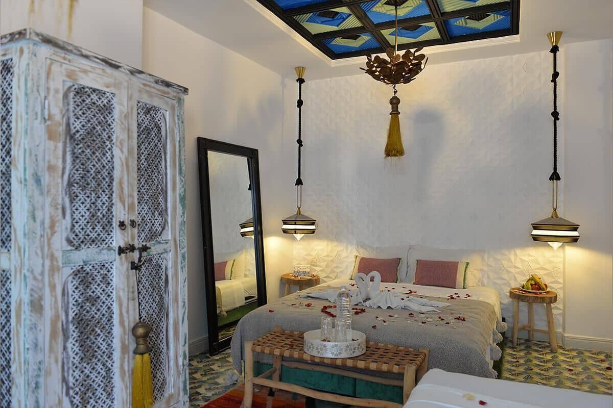 Un dormitorio con cama, mesitas de noche, un espejo y una araña.