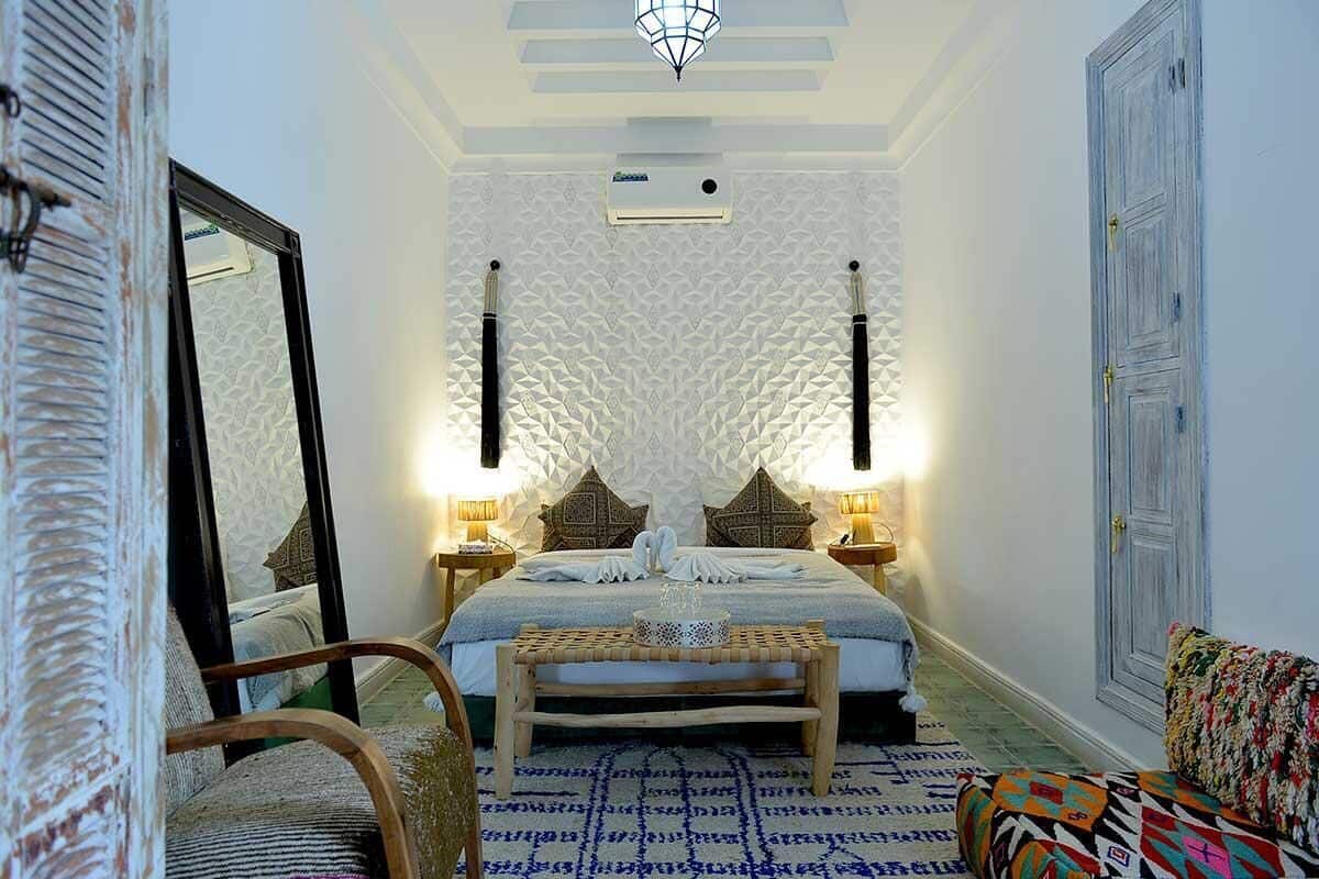 Un dormitorio con cama, lámparas de noche, un banco, un espejo y una puerta.