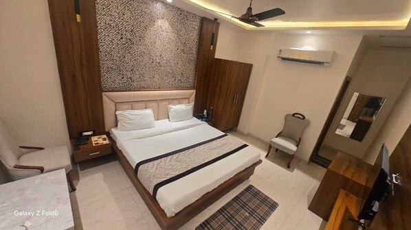 A hotel room with a large bed, a bedside table, a chair, a desk, and a wardrobe. - The Monark Inn (Sandila)