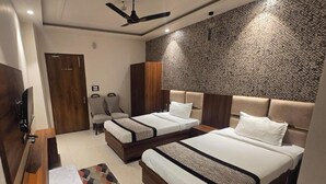 A hotel room with two beds, a desk, a wardrobe, and a ceiling fan. - The Monark Inn (Sandila)