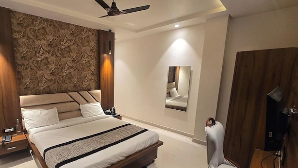 A modern bedroom with a large bed, a ceiling fan, a bedside table, a chair, and a mirror on the wall. - The Monark Inn (Sandila)