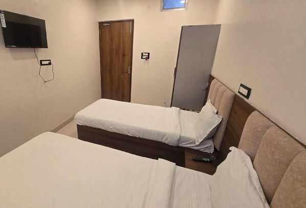 A hotel room with a single bed, a television mounted on the wall, a wooden door, and a wardrobe. - The Monark Inn (Sandila)