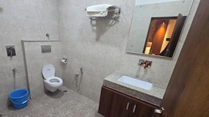 A bathroom with a toilet, sink, and mirror. There is a towel rack above the sink and a blue bucket on the floor. - The Monark Inn (Sandila)