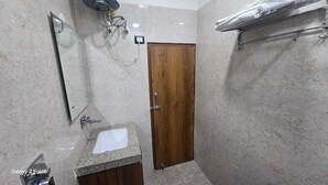 A bathroom with a marble wall, a wooden door, a sink with a mirror, and a towel rack. - The Monark Inn (Sandila)