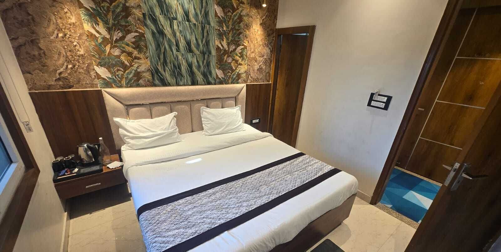 A hotel room with a large bed, a nightstand, a wall mural, and a wooden door.