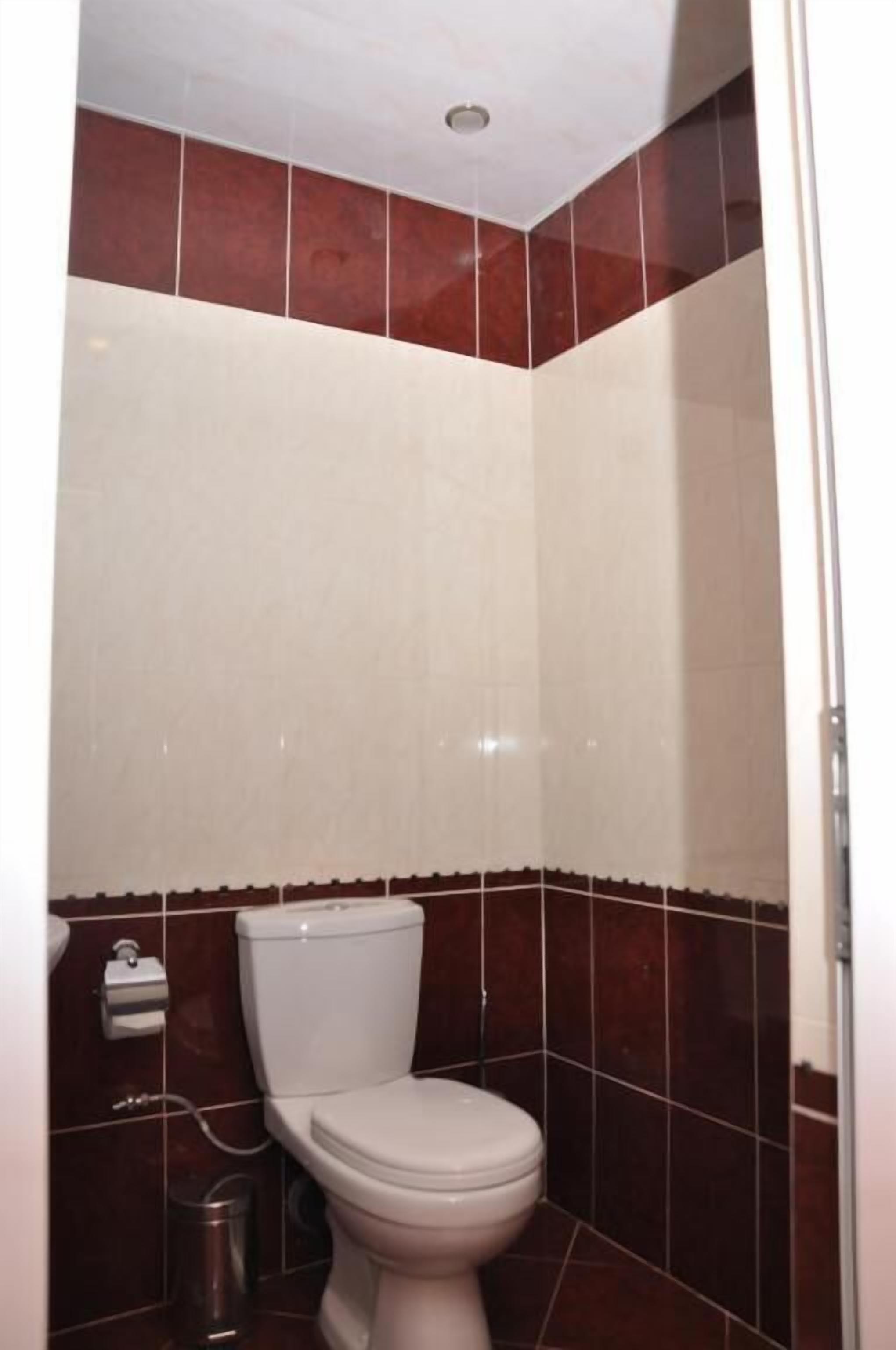 A small, compact bathroom with a white toilet, a trash bin, and a paper towel dispenser.