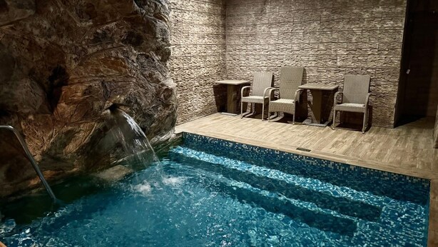 Une piscine intérieure avec un mur en pierre en arrière-plan et une cascade décorative.