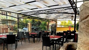 Un espace extérieur aménagé en terrasse, avec des tables et des chaises, un élément décoratif en pierre et une clôture en métal.