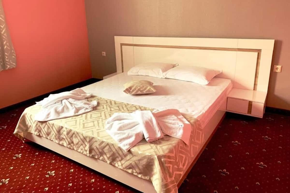 A neatly made bed with a patterned bedspread, two pillows, and two towels on the floor.