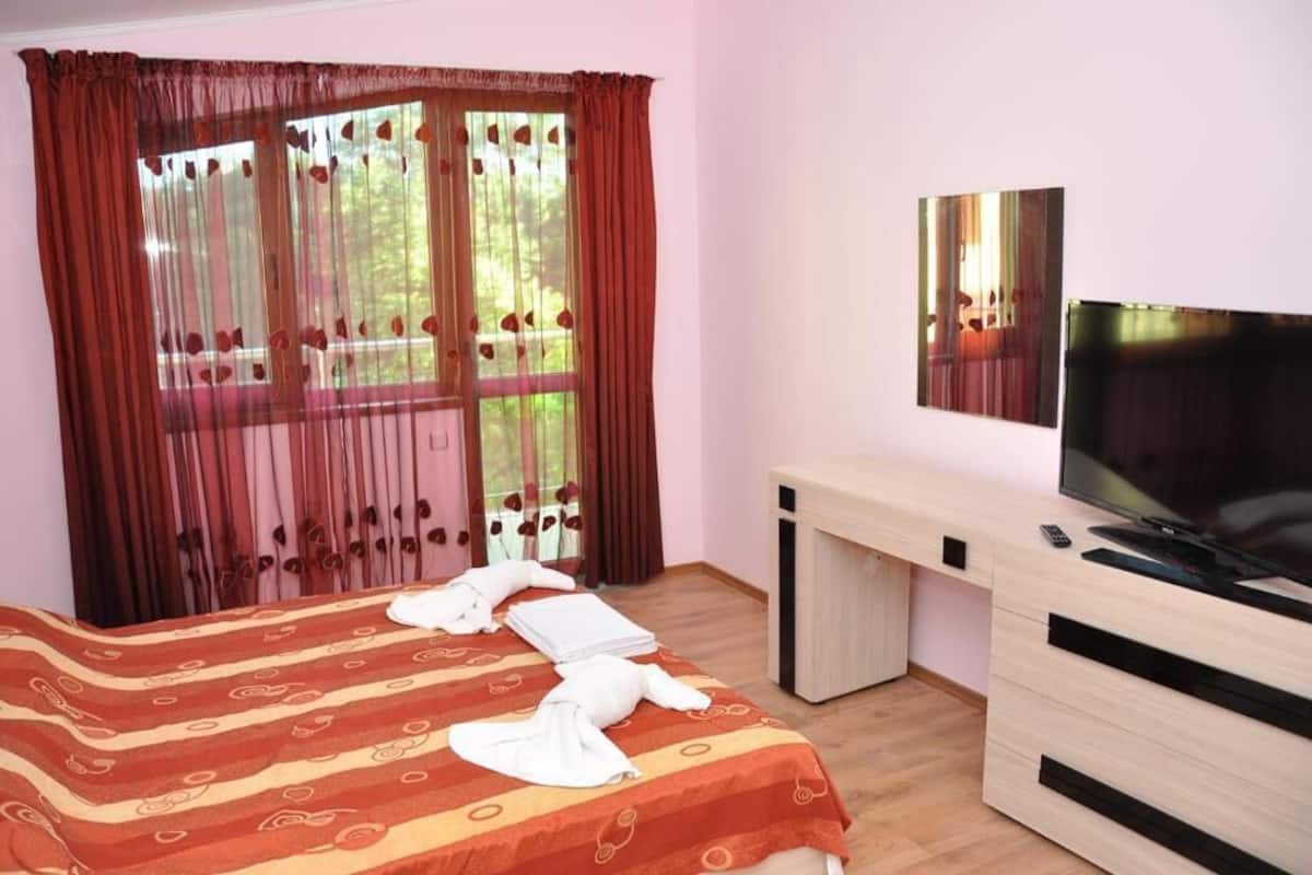 A hotel room with a bed, a desk with a TV, and a window with curtains.