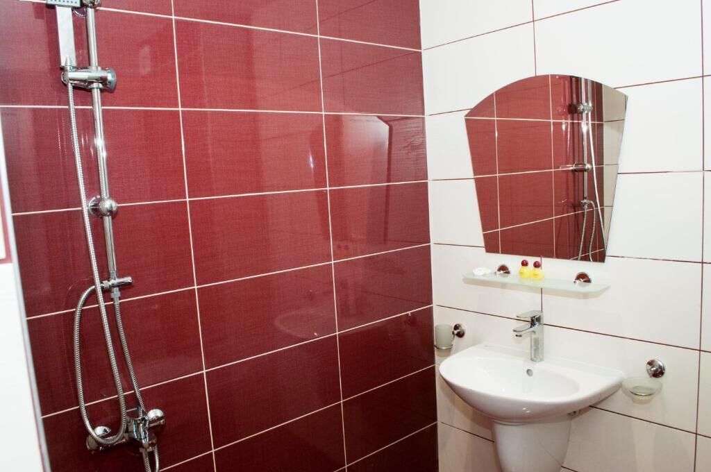 Une salle de bain avec des murs recouverts de carreaux rouges, un lavabo blanc et un miroir au-dessus.