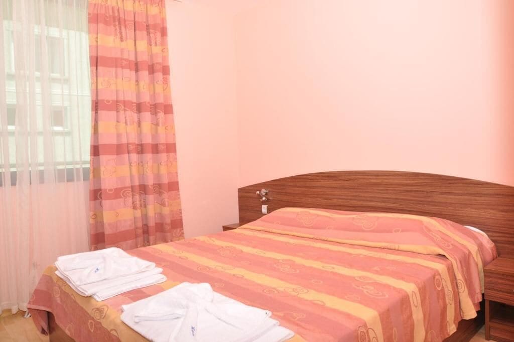 Uma cama de solteiro com cabeceira de madeira, colcha listrada e toalhas brancas no chão.