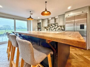 A modern kitchen with a wooden island, bar stools, stainless steel appliances, and pendant lighting.