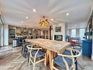 Eine moderne Küche mit eingebauten Backöfen, ein Essbereich mit Holztisch und Stühlen sowie ein Wohnzimmer mit Sofa und Fernseher.