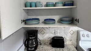 Una cocina con armarios blancos, encimera de granito, cafetera, tostadora y estufa.
