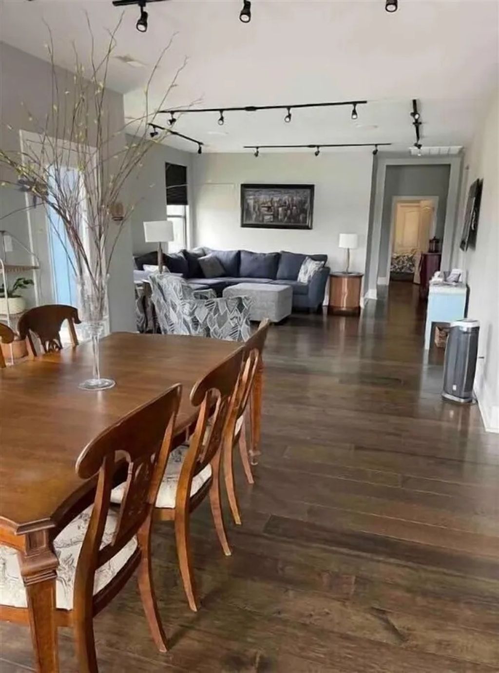 A spacious dining area with a wooden table and chairs, a gray sofa, and a large window.