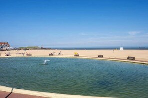 Una passeggiata lungomare con una fontana, panchine e una spiaggia di sabbia.
