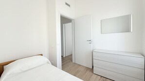 A bedroom with a bed, a dresser, a mirror, and a door leading to another room. - SE202 - Senigallia, new, fully equipped three-room apartment in the city center (Senigallia)