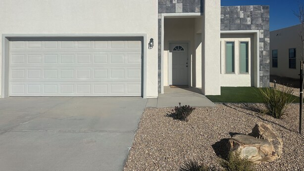 Une maison moderne à deux étages, dotée d’une porte de garage blanche, d’une façade en pierre et d’une pelouse bien entretenue.