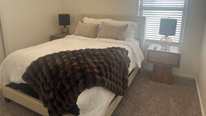Une chambre à coucher avec un lit, deux tables de chevet, une lampe et une fenêtre avec des stores.