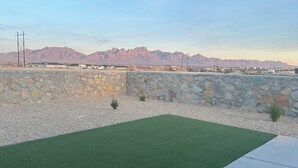 Un espace aménagé avec une pelouse artificielle, un mur en pierre et une vue sur les montagnes en arrière-plan.