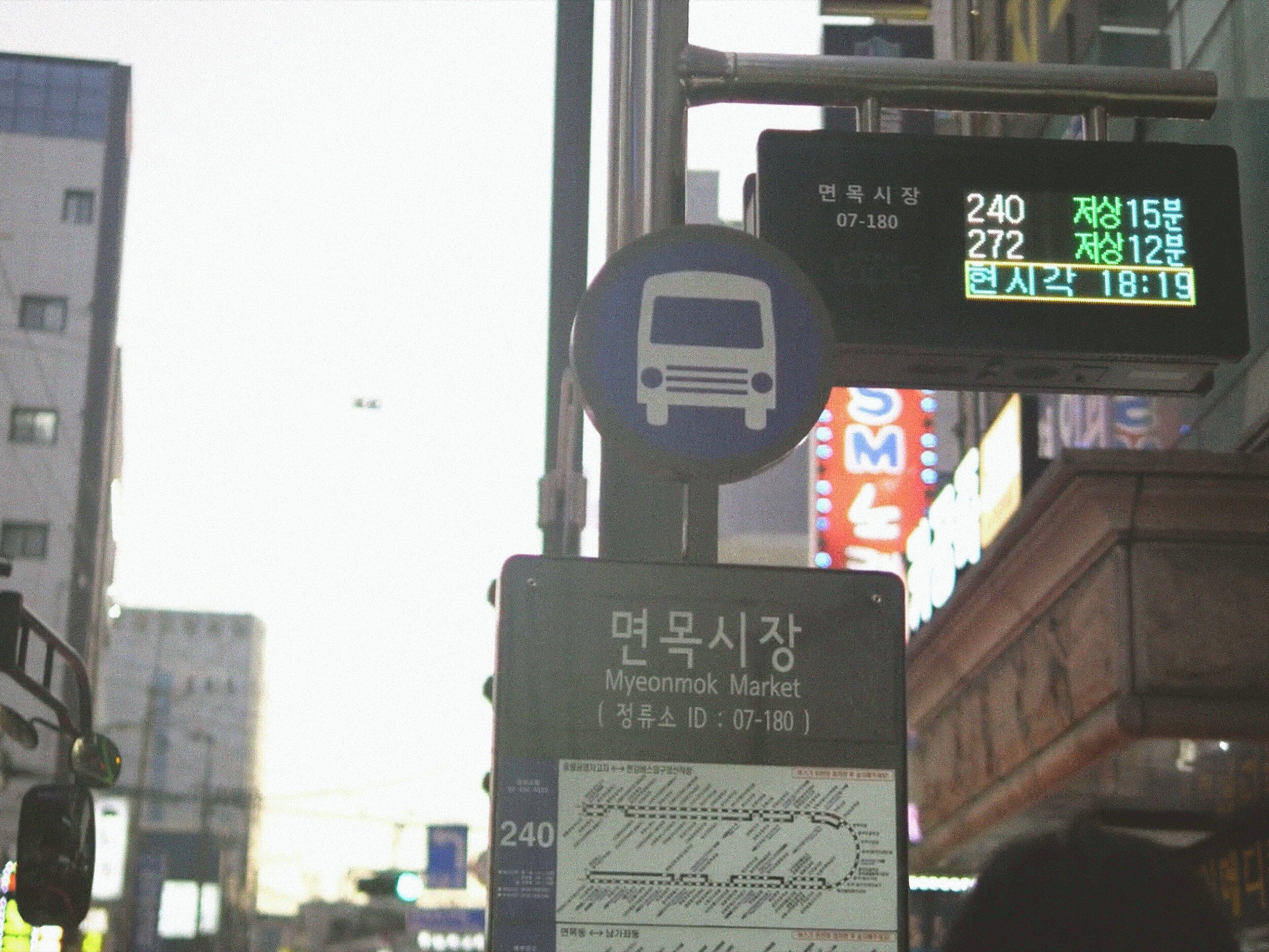Una señal de parada de autobús con información de ruta y un cartel que indica el Mercado Myemunmok.