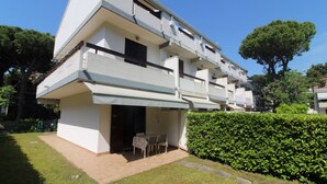 Un moderno edificio residencial de varios pisos con techo plano, un área de estar exterior cubierta y un jardín bien cuidado.