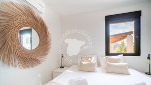 Een slaapkamer met een grote ronde spiegel, een bed met witte lakens en een raam met uitzicht op het landschap.