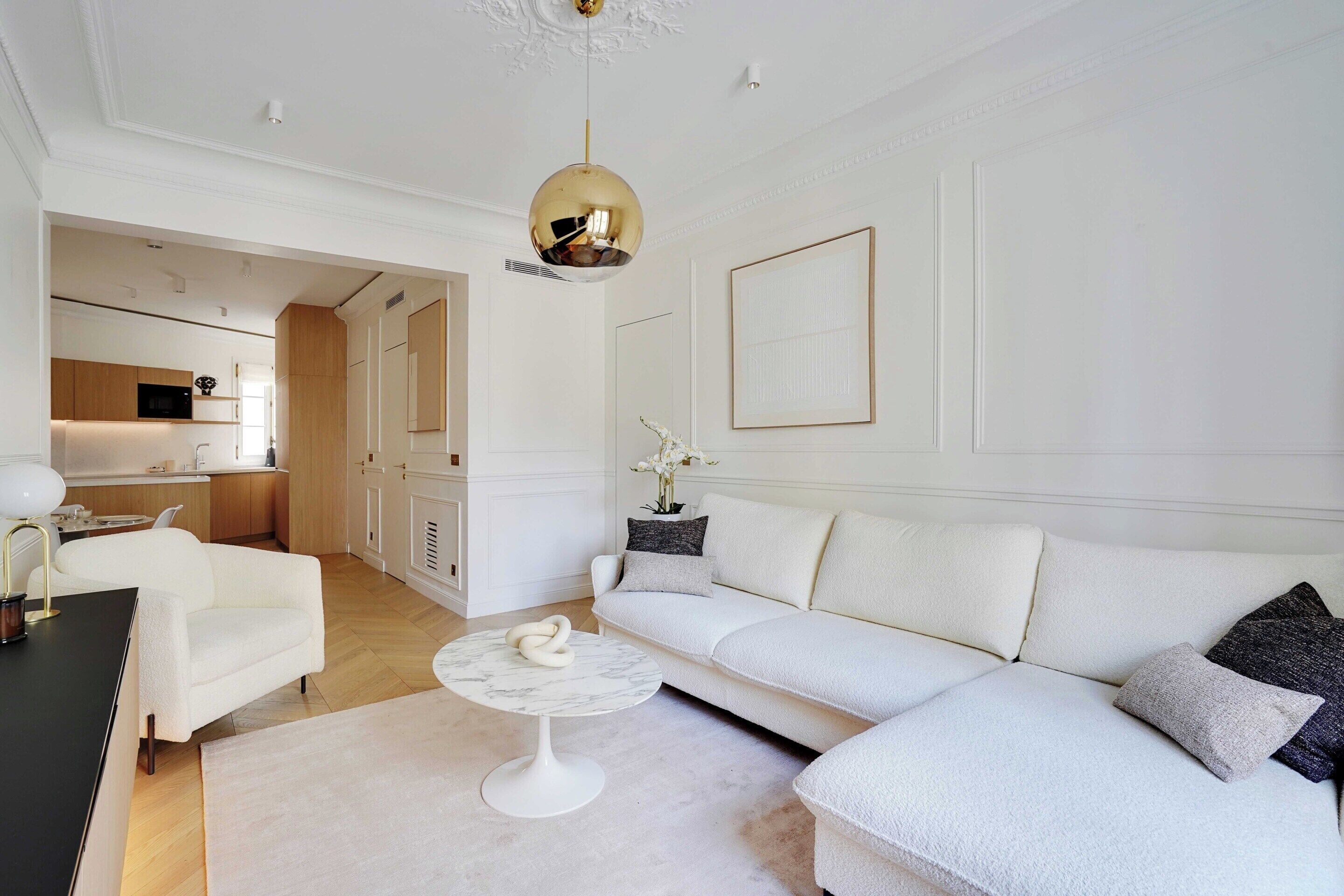 A modern living room with a white sofa, a round coffee table, and a kitchen in the background.